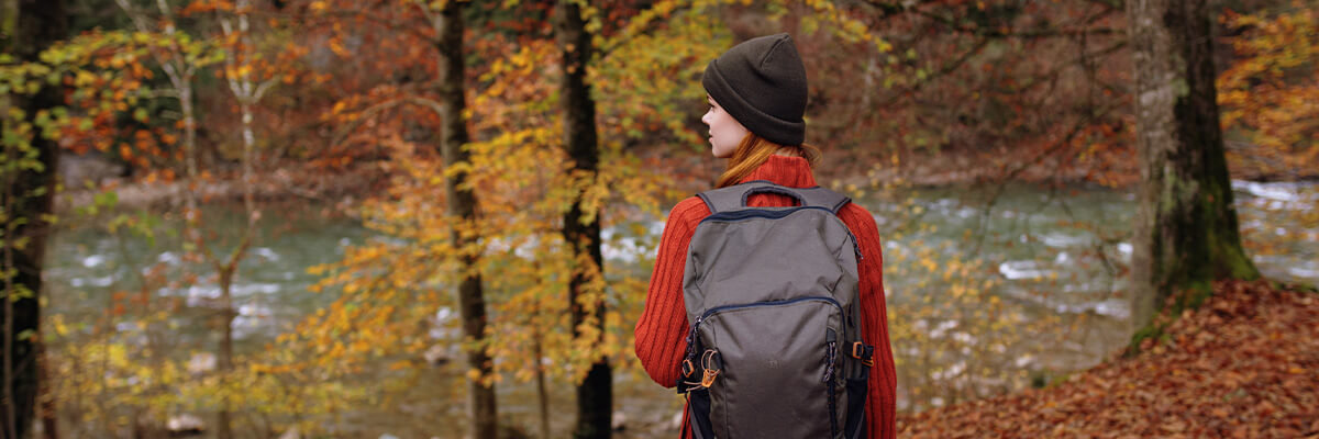 Woman hiking beside river, surrounded by beautiful fall leaves.